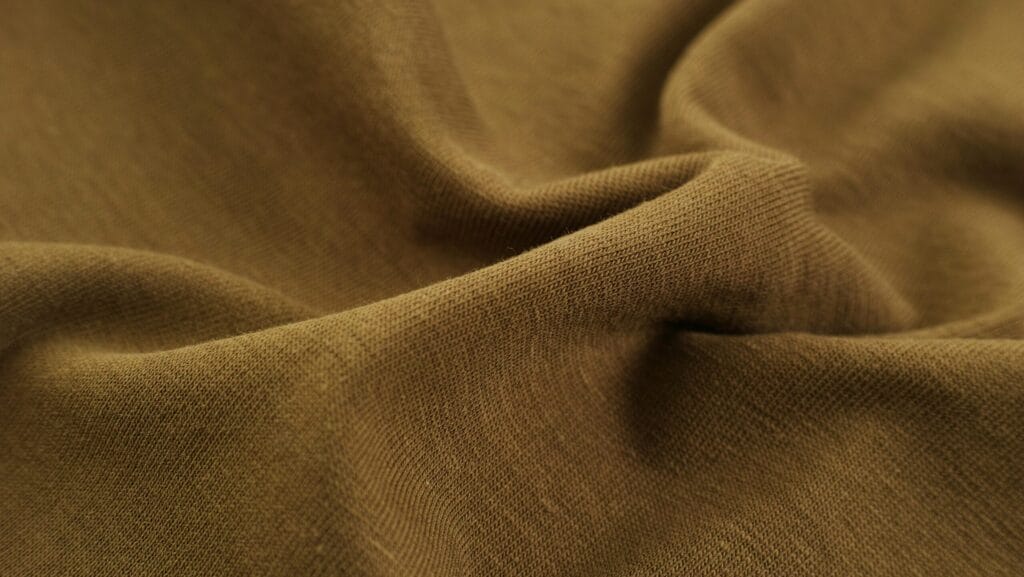 Brownish-olive fabric with visible texture and folds, representing textile sourcing in apparel manufacturing