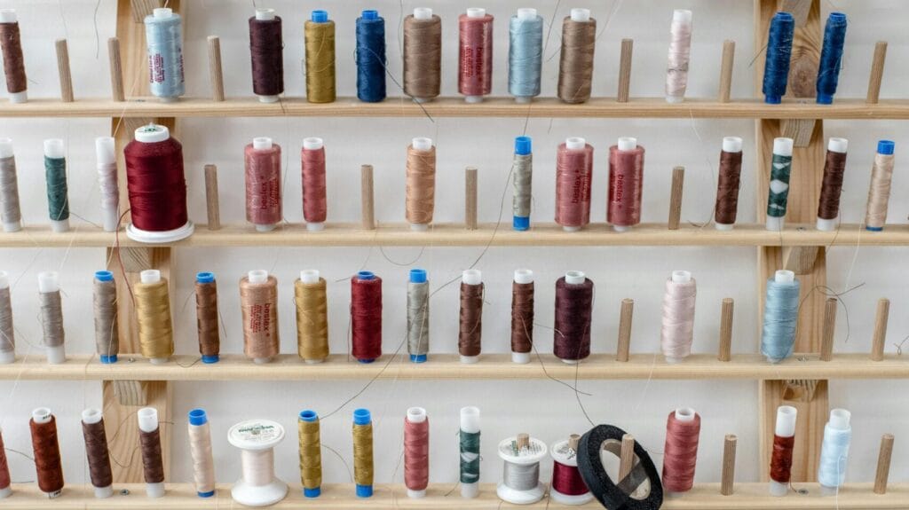 Wall-mounted thread rack with colorful spools representing garment production and compliance standards