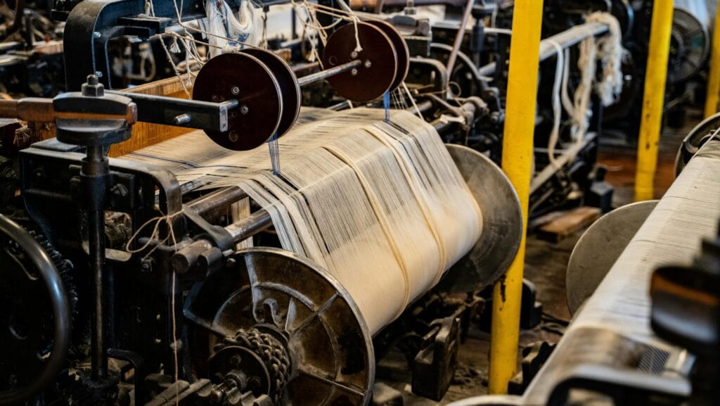 Industrial textile weaving machine with spools and threads, symbolizing precision in garment production