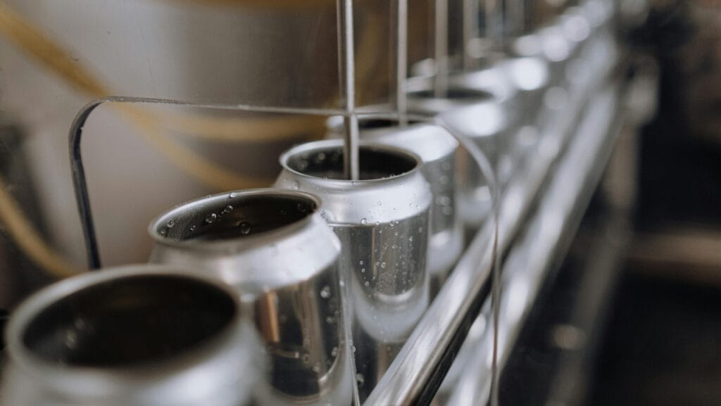 Close-up of beverage canning production line with aluminum cans being filled by automated nozzles