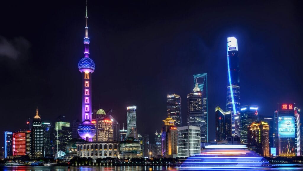 Shanghai skyline at night with Oriental Pearl Tower, modern skyscrapers, and illuminated boat on Huangpu River