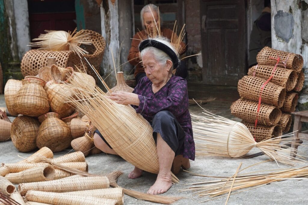 Vietnamese artisan in a conical hat hand-weaving rattan baskets surrounded by finished woven handicraft products